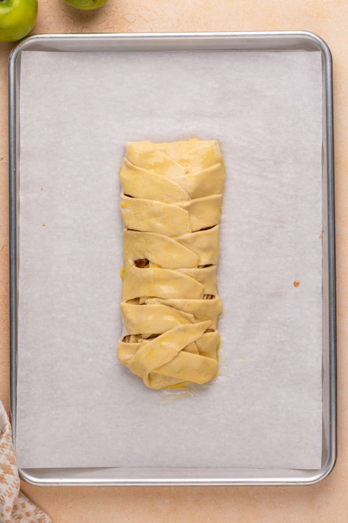 Egg washed puff pastry apple strudel on a baking sheet, ready to go in the oven.