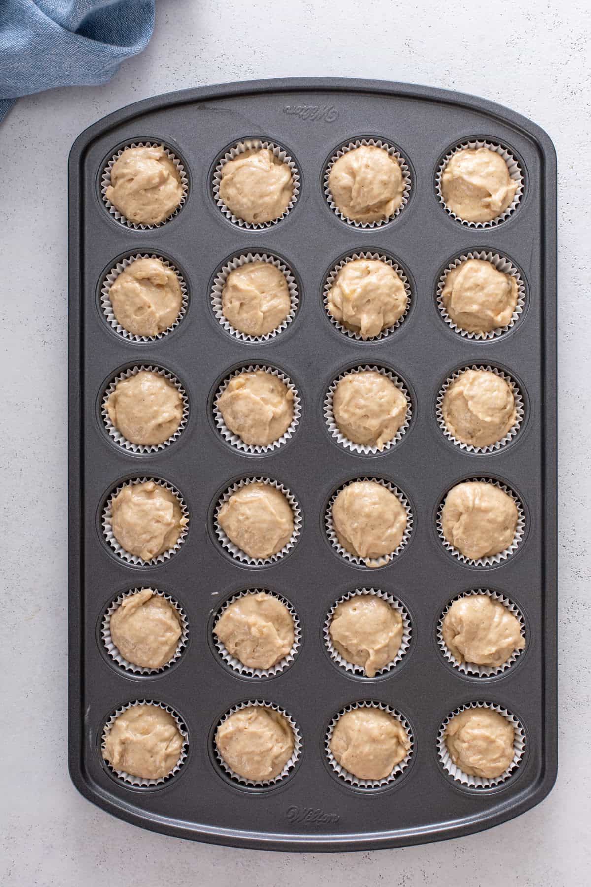 Unbaked mini banana muffins in a tin, ready to go in the oven.
