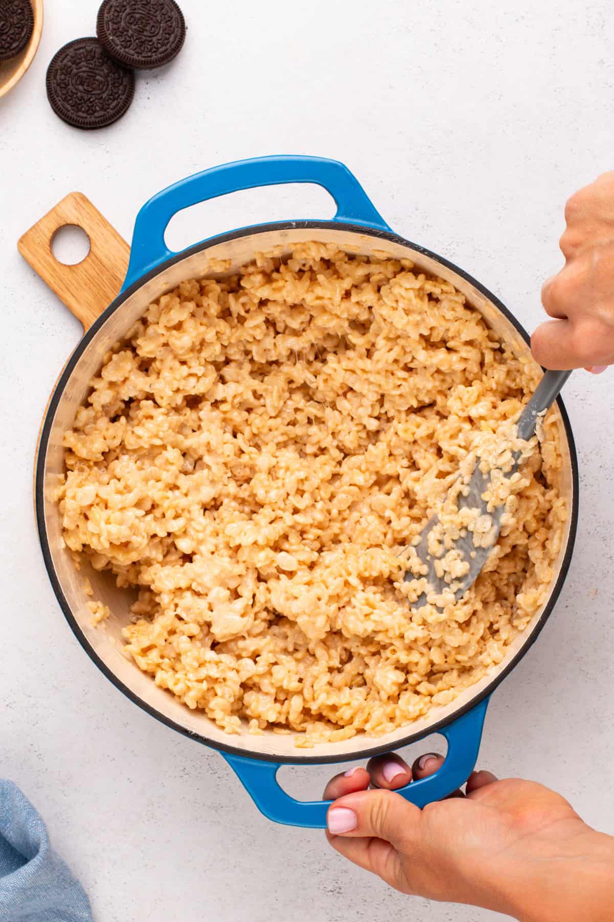 Person stirring crispy rice cereal into melted marshmallow mixture in a dutch oven.