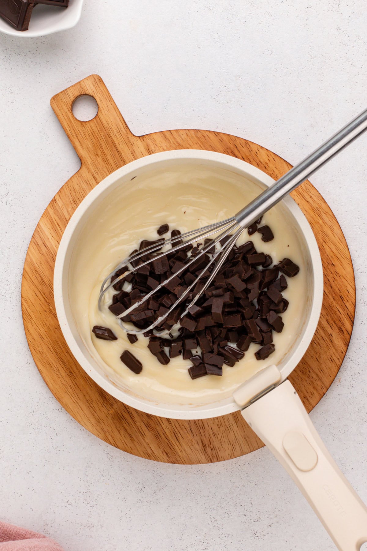 Chopped chocolate being added to hot pudding base in a saucepot.