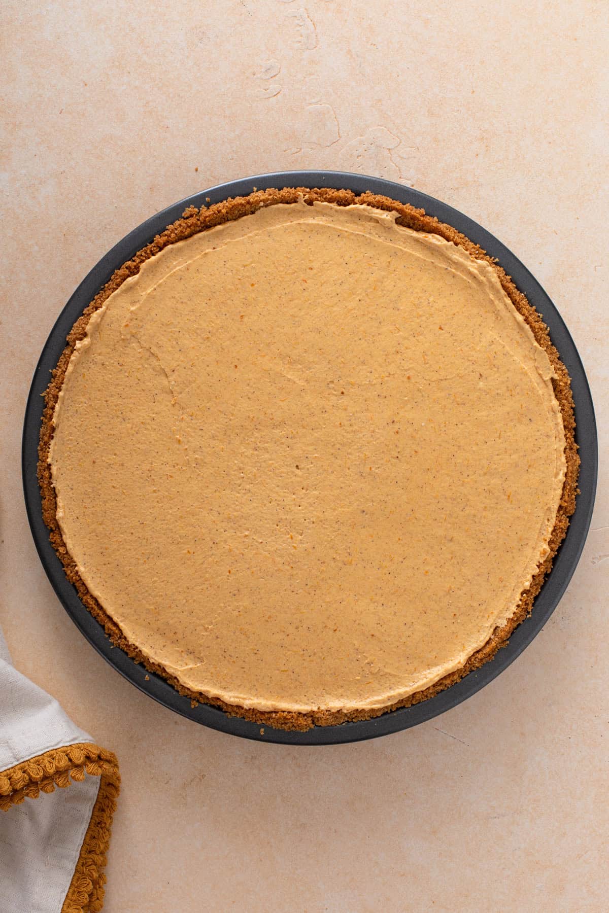 Filling for no-bake pumpkin cheesecake pie spread into a graham cracker crust.