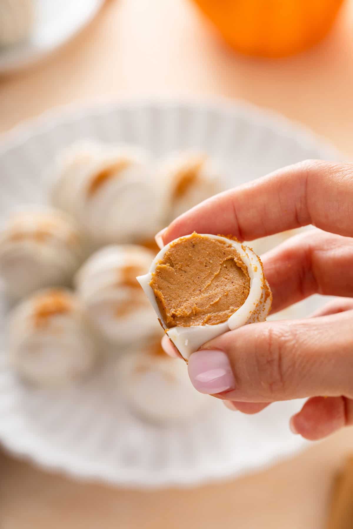 Person holding up a pumpkin cheesecake ball with a bite taken from it.