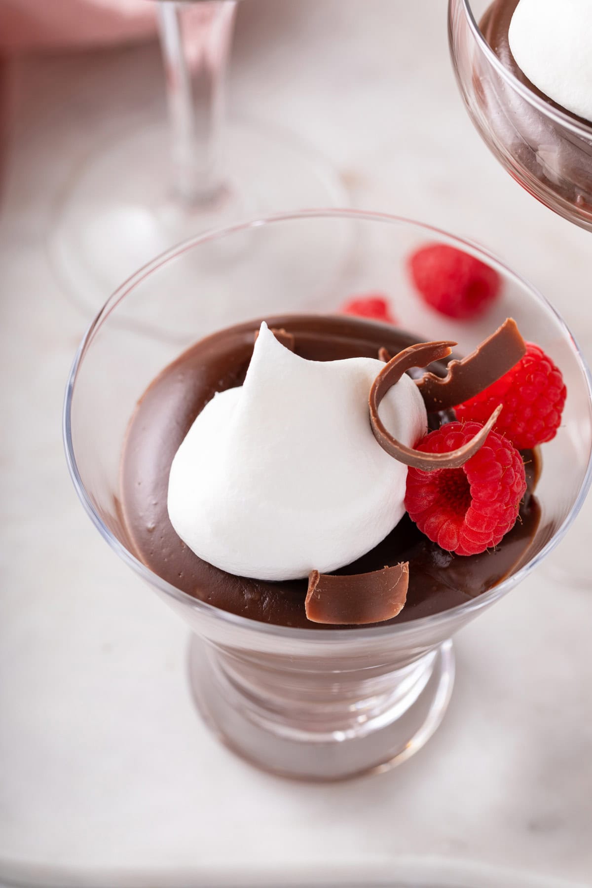 Chocolate pudding in a glass serving dish, topped with whipped cream and fresh raspberries.