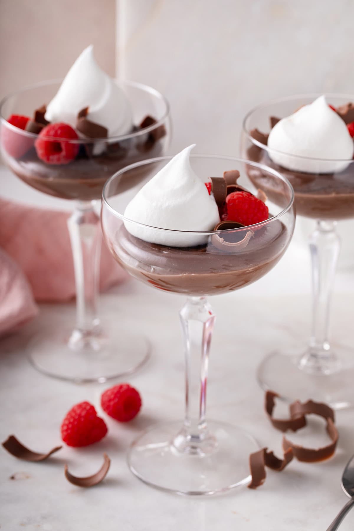 Side view of three coupe glasses filled with homemade chocolate pudding and garnished with whipped cream and fresh berries.