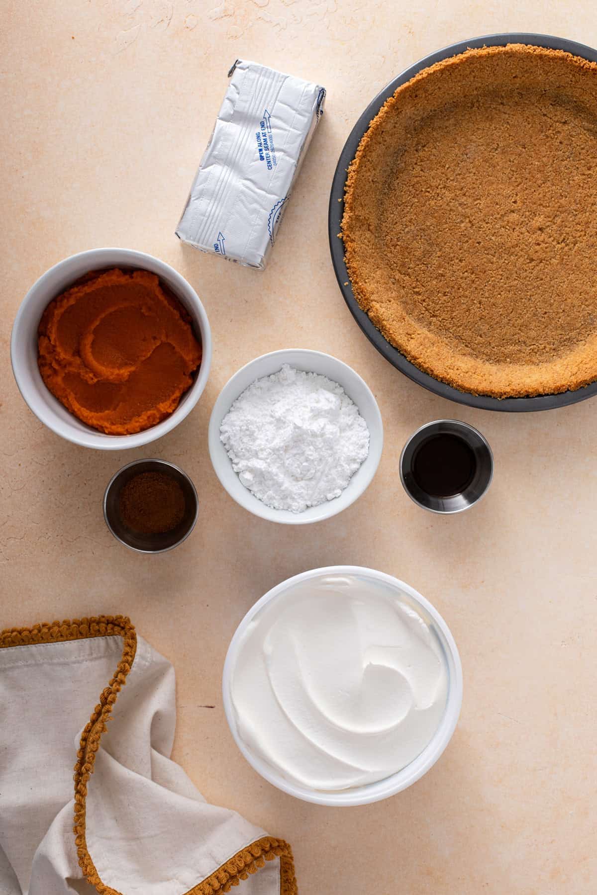 Ingredients for no-bake pumpkin cheesecake pie arranged on a countertop.