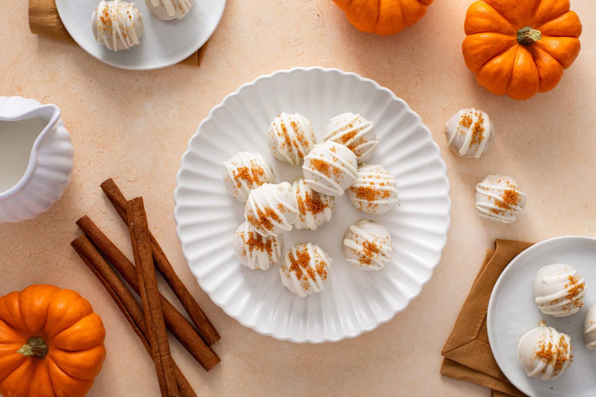 Overhead view of several no-bake pumpkin cheesecake balls arranged on a white plate.