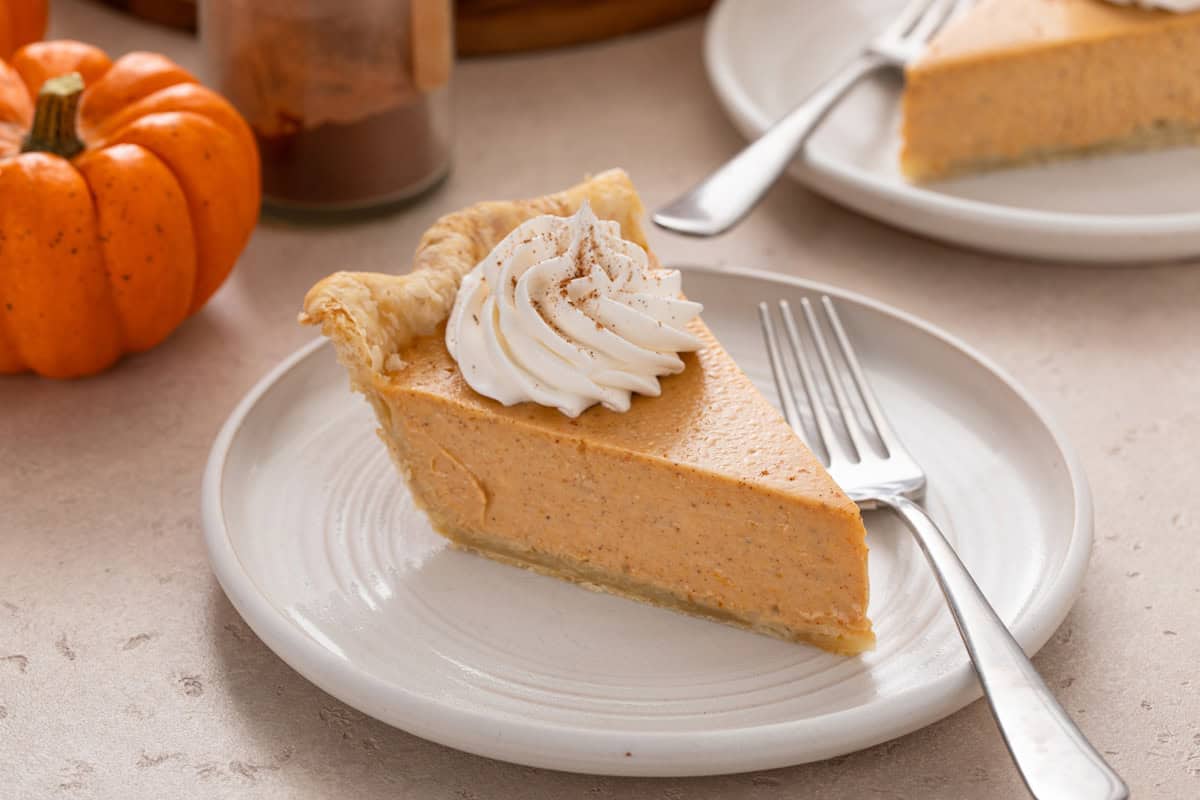 Slice of pumpkin cheesecake pie next to a fork on a white plate.