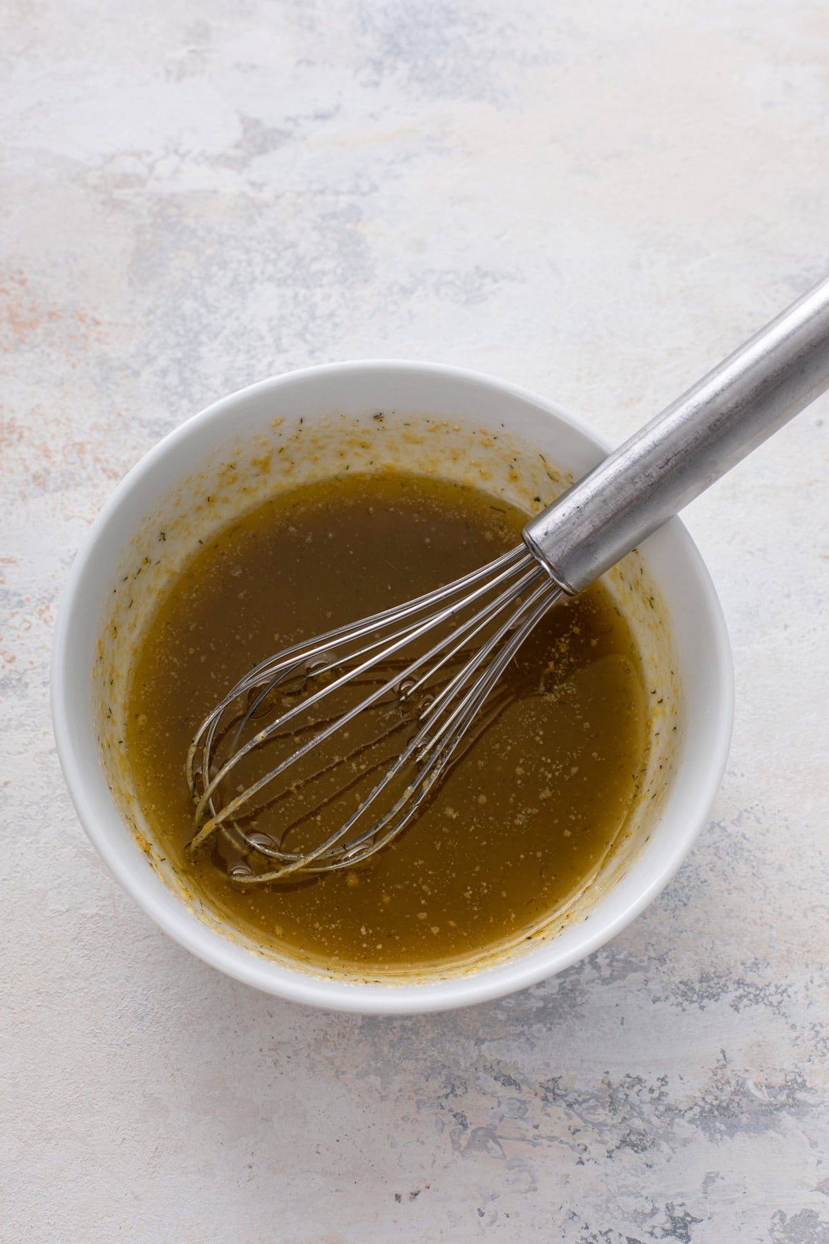 Melted butter and ranch chex mix seasoning mixed in a small white bowl.