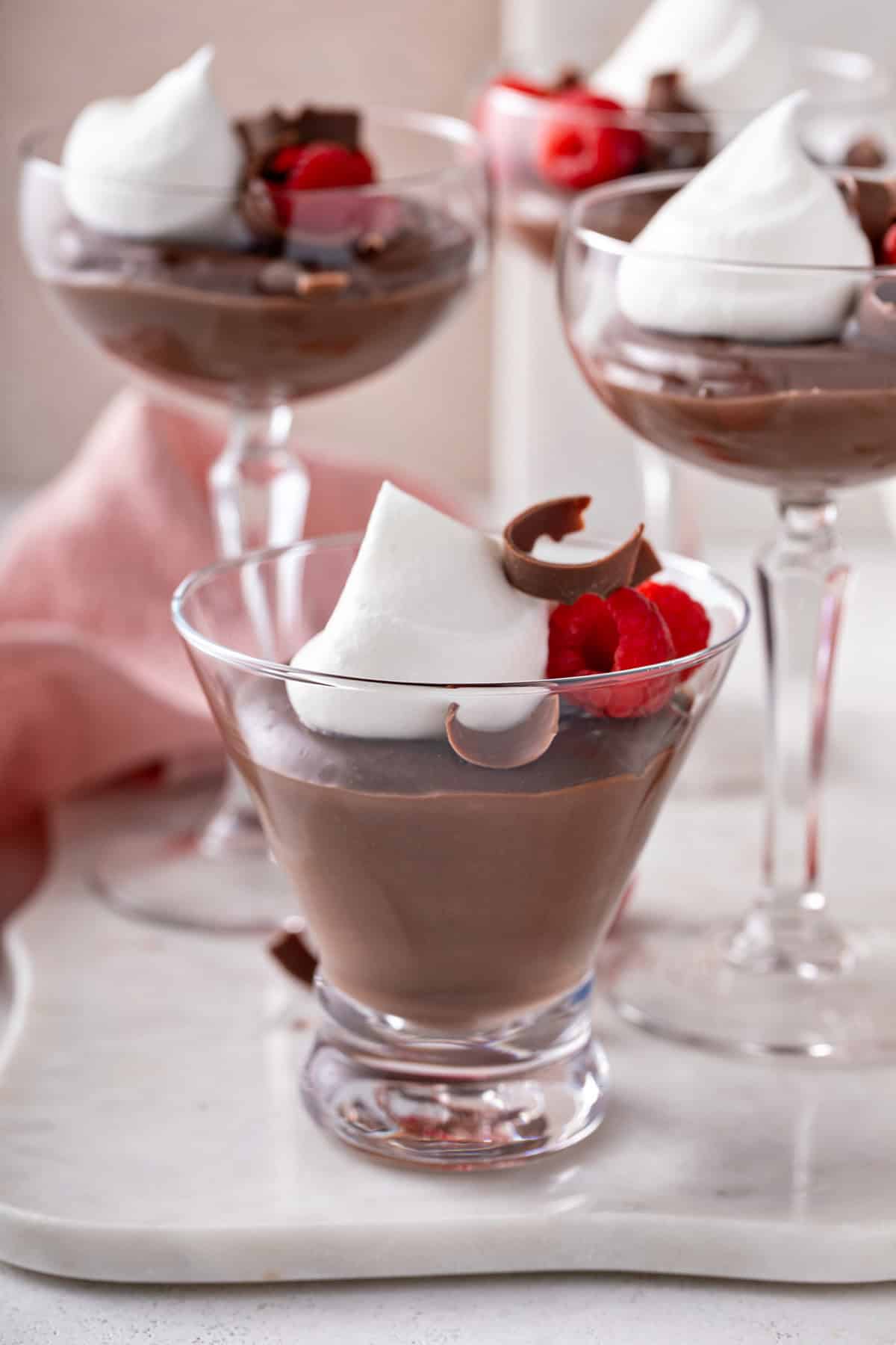 Three glasses filled with servings of chocolate pudding and topped with whipped cream and fresh raspberries.