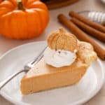 Plated slice of pumpkin cheesecake pie topped with a pumpkin-shaped cookie.