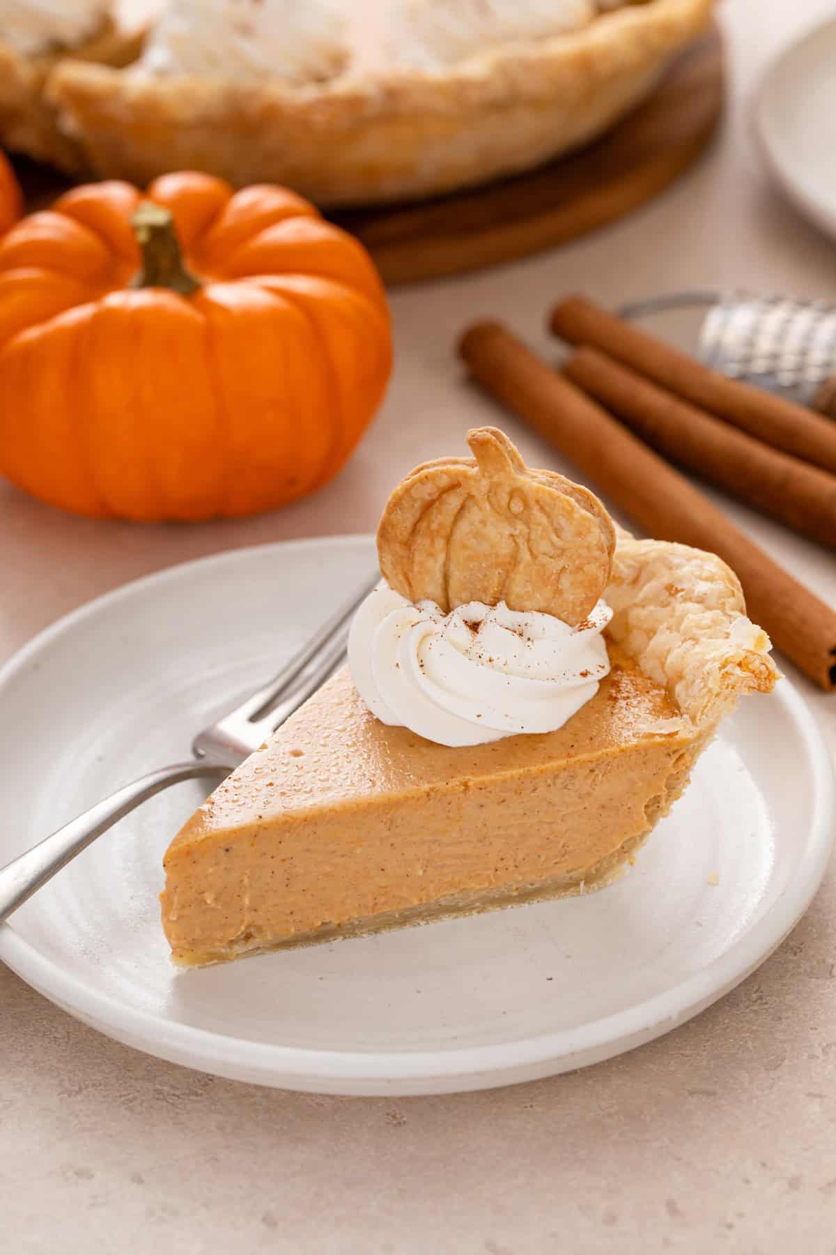 Slice of pumpkin cheesecake pie garnished with whipped cream and a pumpkin-shaped cookie.