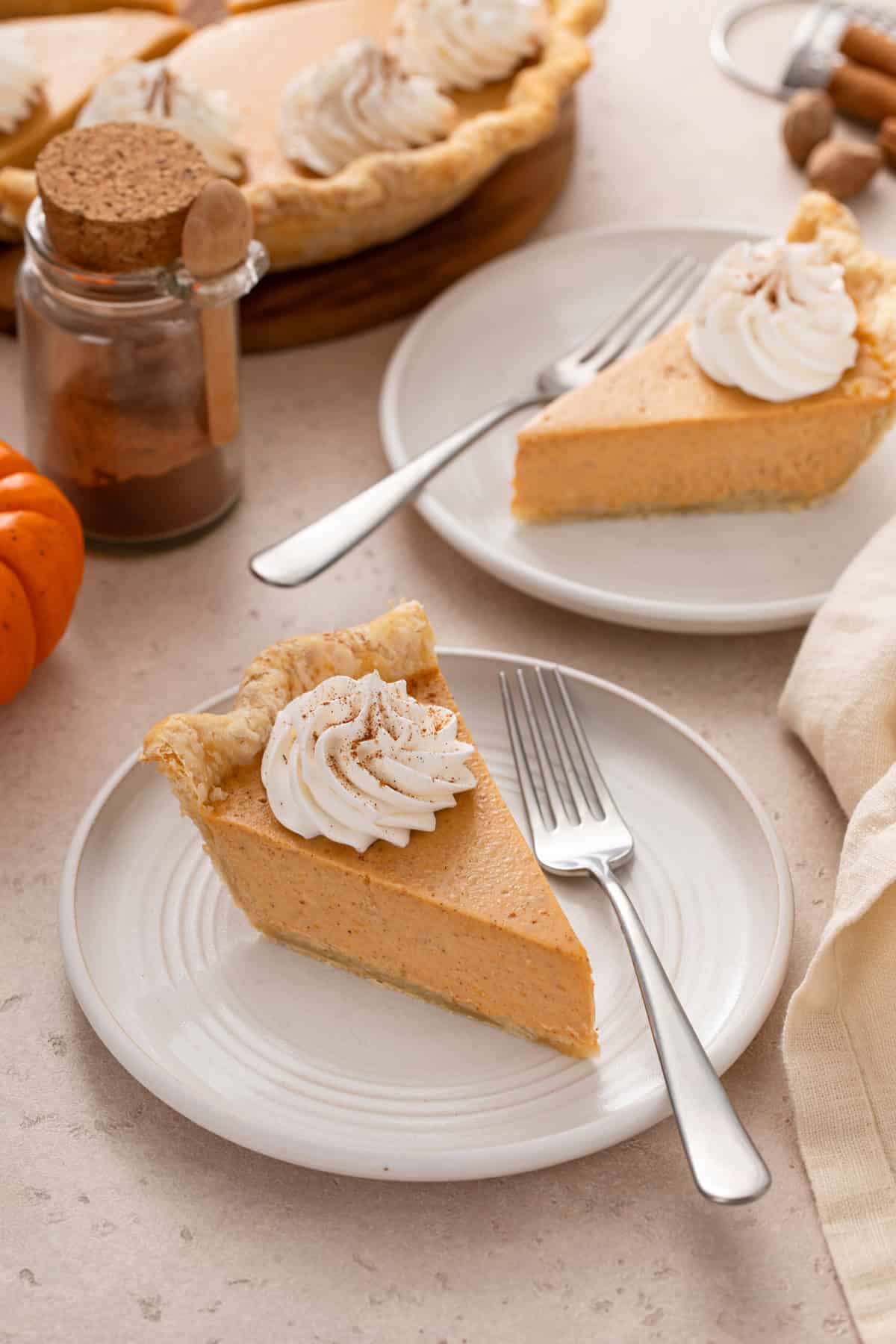 Two white plates, each holding a fork and a slice of pumpkin cheesecake pie.