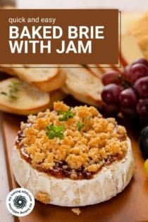 Wheel of baked brie with jam on a wooden board with fruit and baguette slices in the background. Text overlay includes recipe name.
