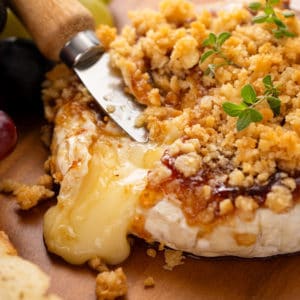 Knife in a wheel of baked brie with jam.