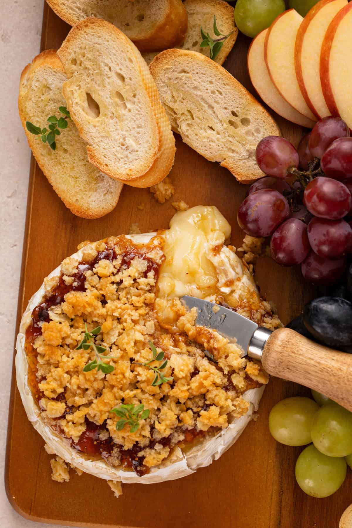 Overhead view of a cheese knife cutting into baked brie with jam.