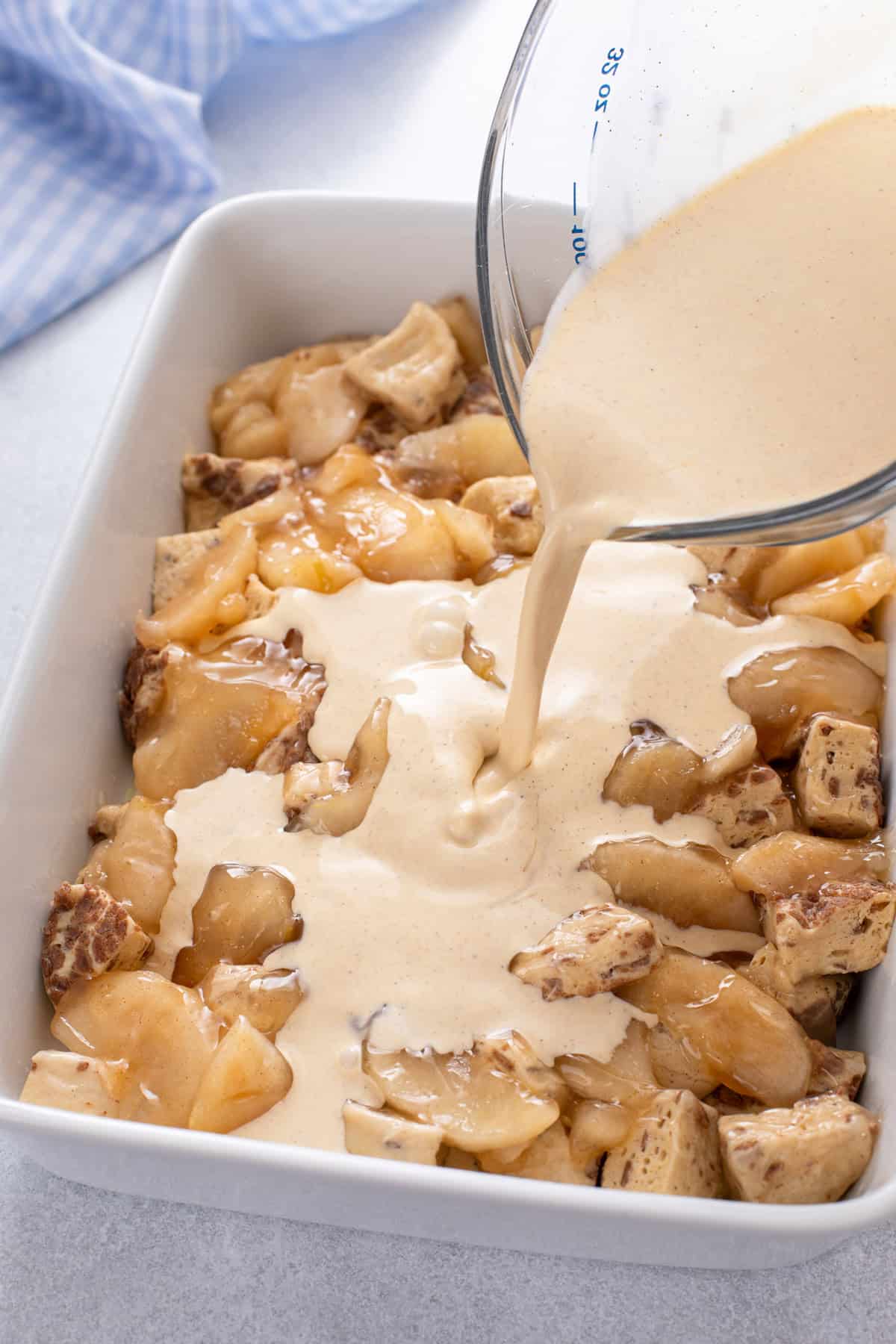 Custard being poured over cinnamon roll pieces and apple pie filling.