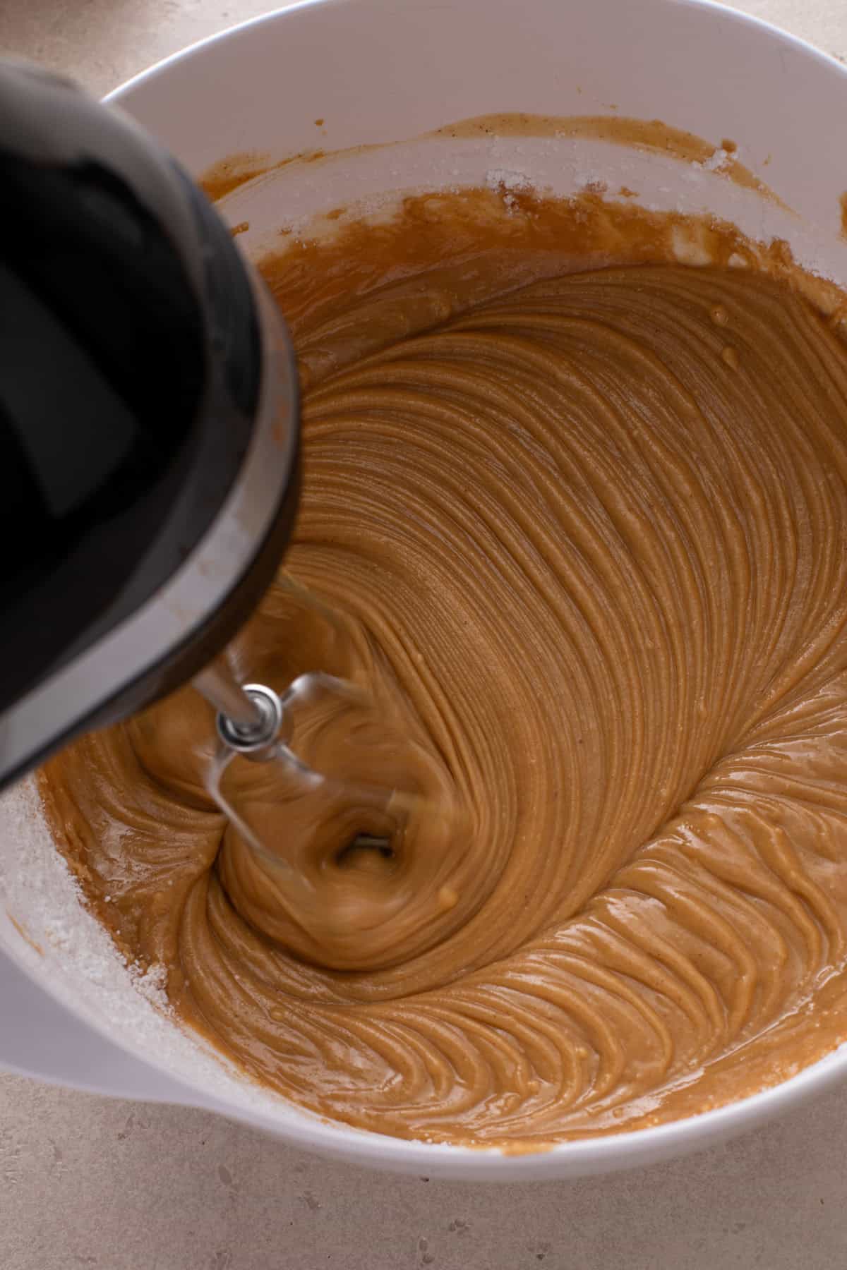 Sugar being added to peanut butter mixture with an electric mixer.