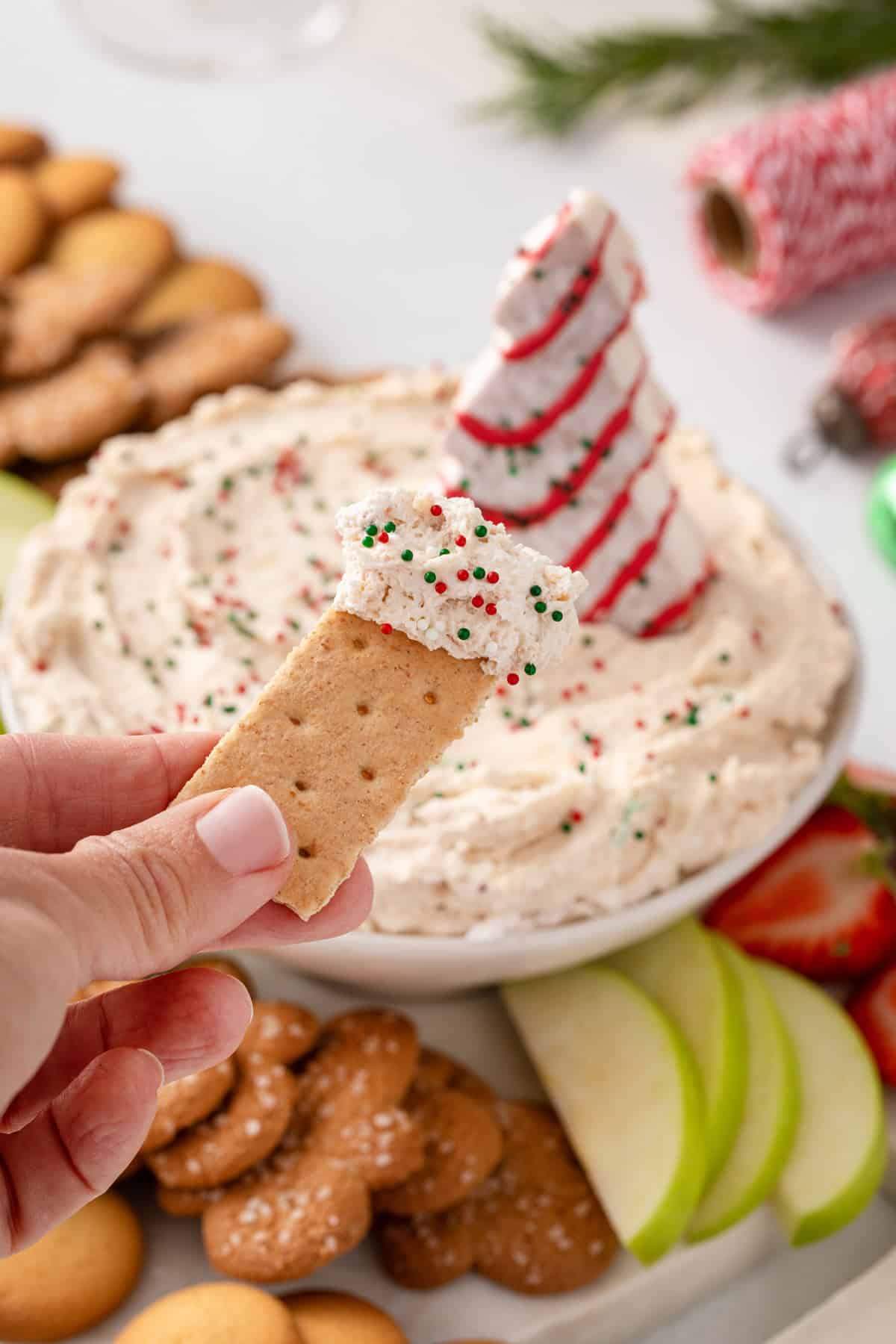 Person holding up a graham cracker dipped in christmas tree cake dip.