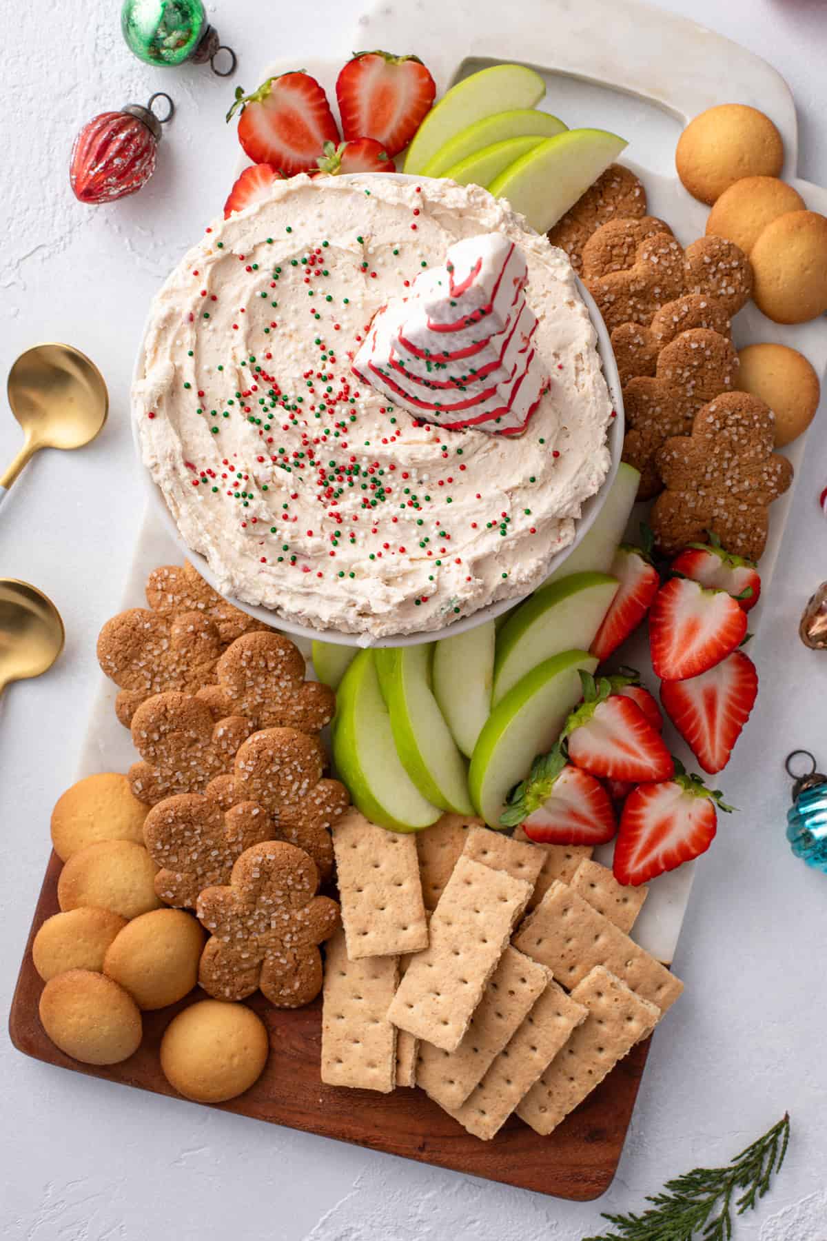 Overhead view of a platter holding cookies, fruit, and a bowl of christmas tree cake dip.