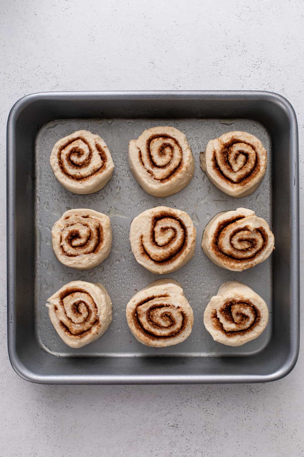 Sliced biscuit cinnamon rolls arranged in a baking pan.