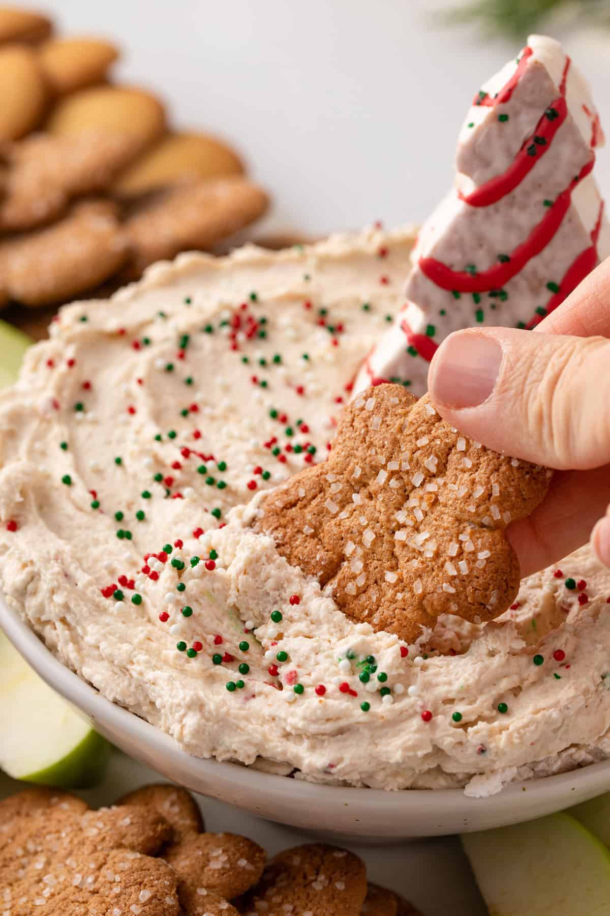 Person dipping a gingersnap cookie into a bowl of christmas tree cake dip.