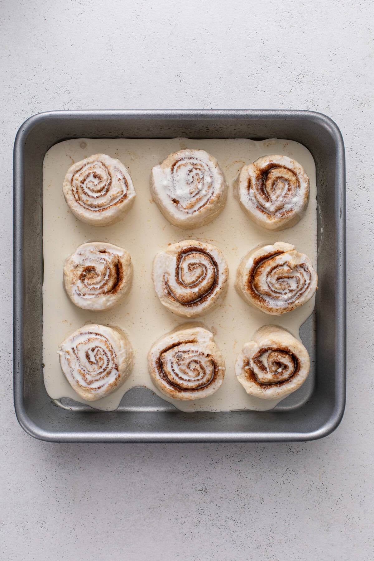Heavy cream poured over biscuit cinnamon rolls in a baking pan, ready to go in the oven.