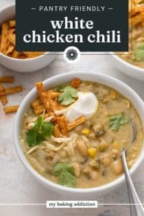 Spoon in a bowl of white chicken chili garnished with sour cream, cilantro, and tortilla strips. Text overlay includes recipe name.