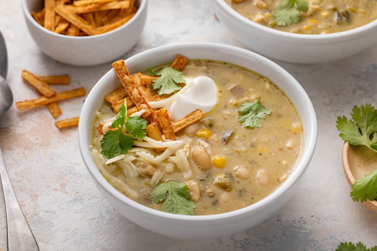 White bowl filled with white chicken chili, garnished with sour cream, cheese, and tortilla strips.