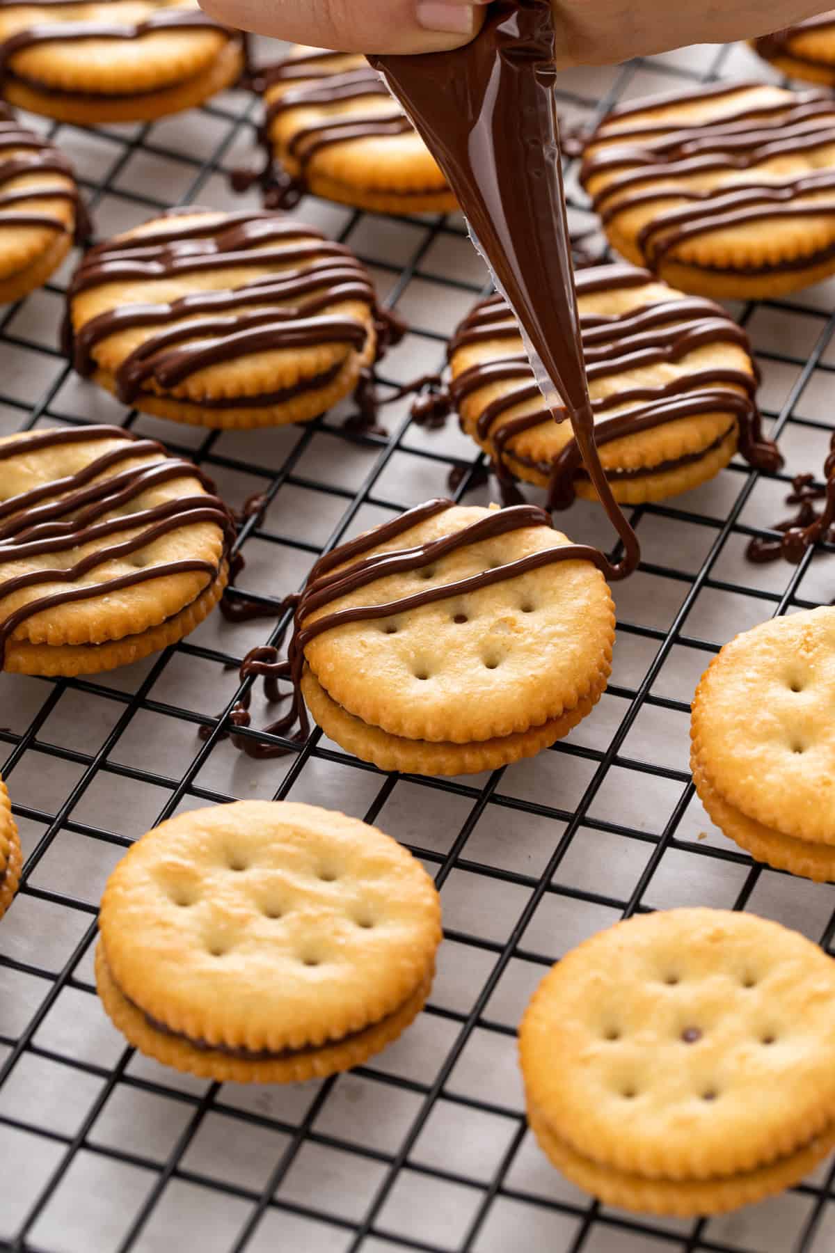 Chocolate being drizzled over ritz cracker sandwich cookies with a piping bag.