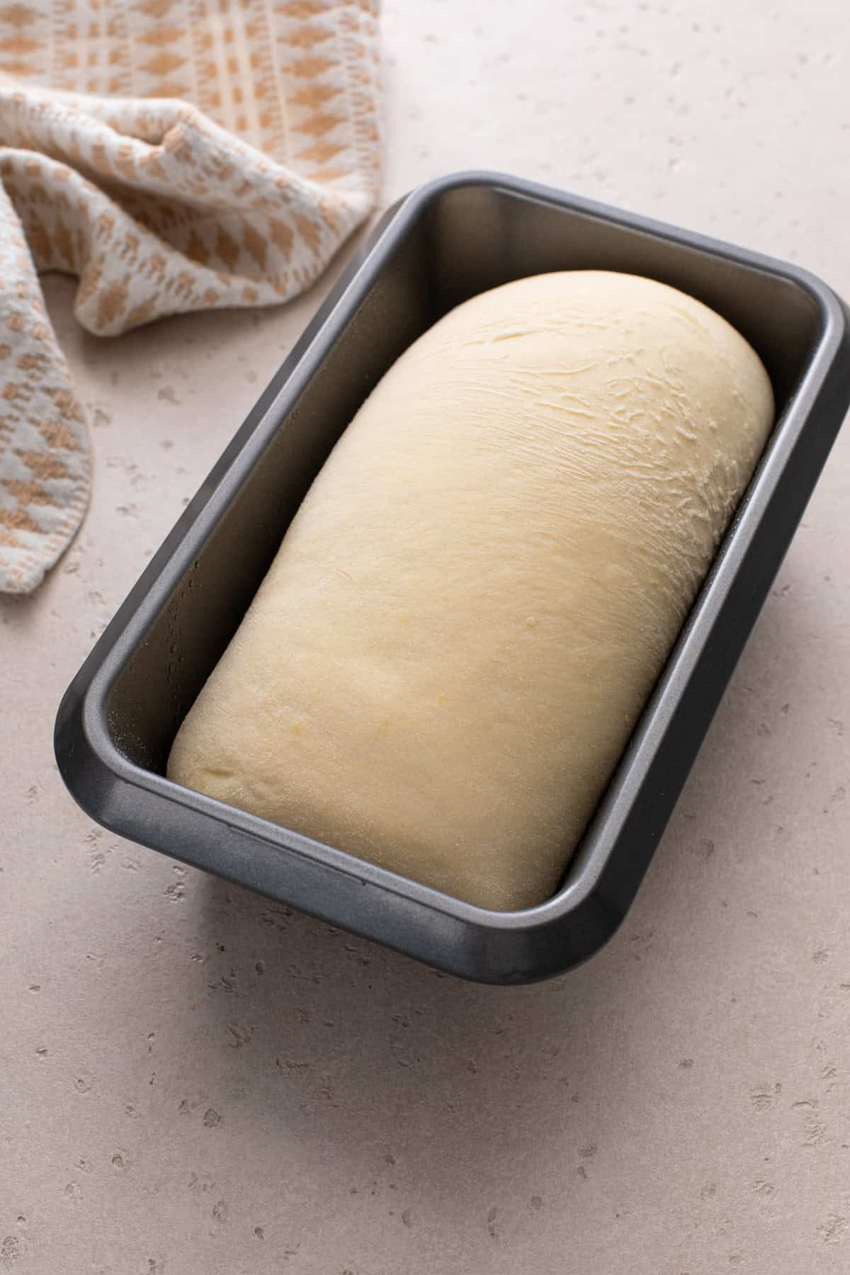 Risen loaf of potato bread in a loaf pan, ready to go in the oven.