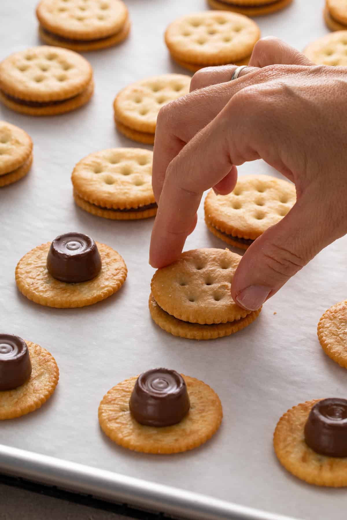Person sandwiching rolos between ritz crackers on a baking sheet.
