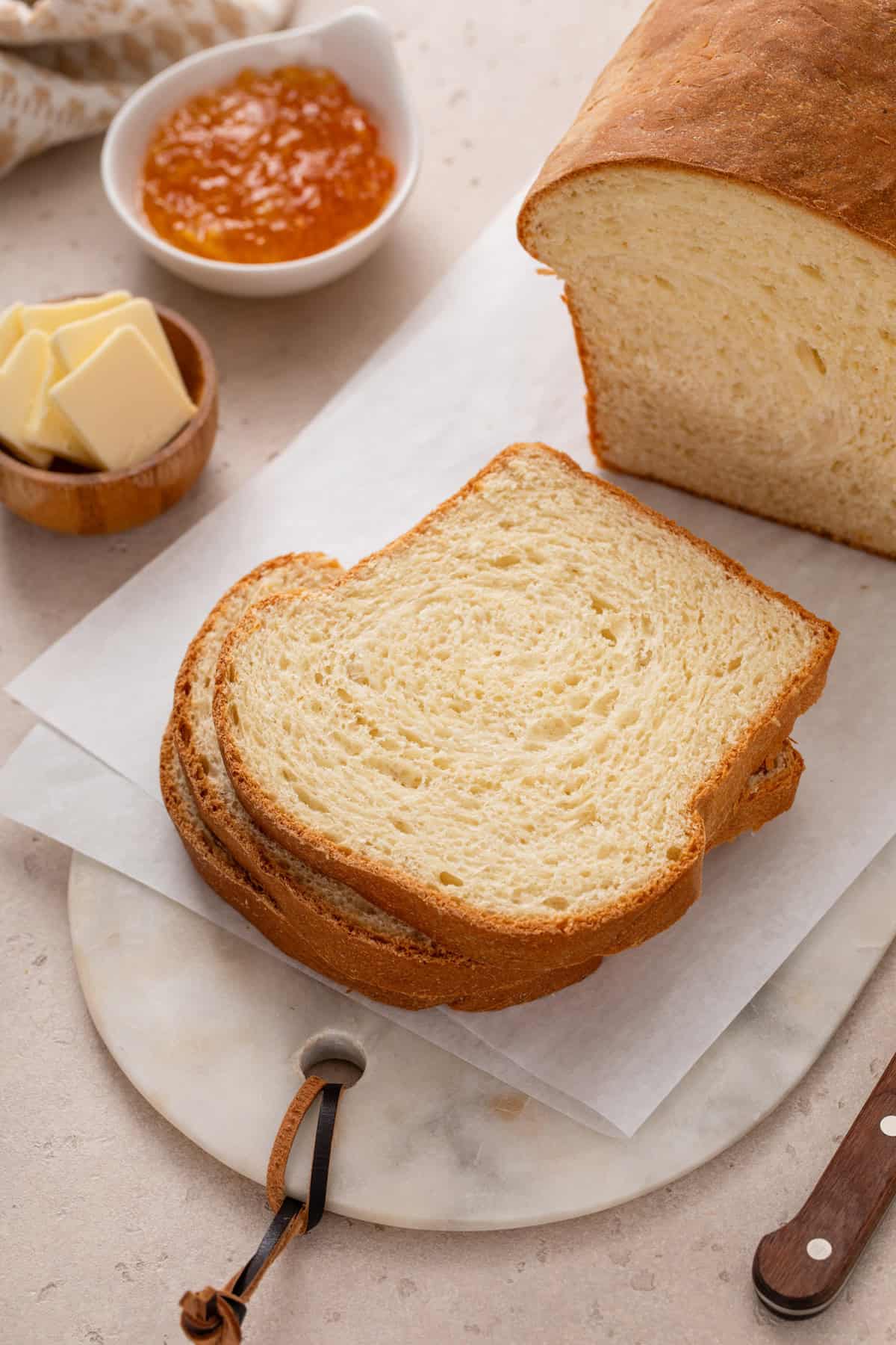 Slices of potato bread on a cutting board next to butter and jam.