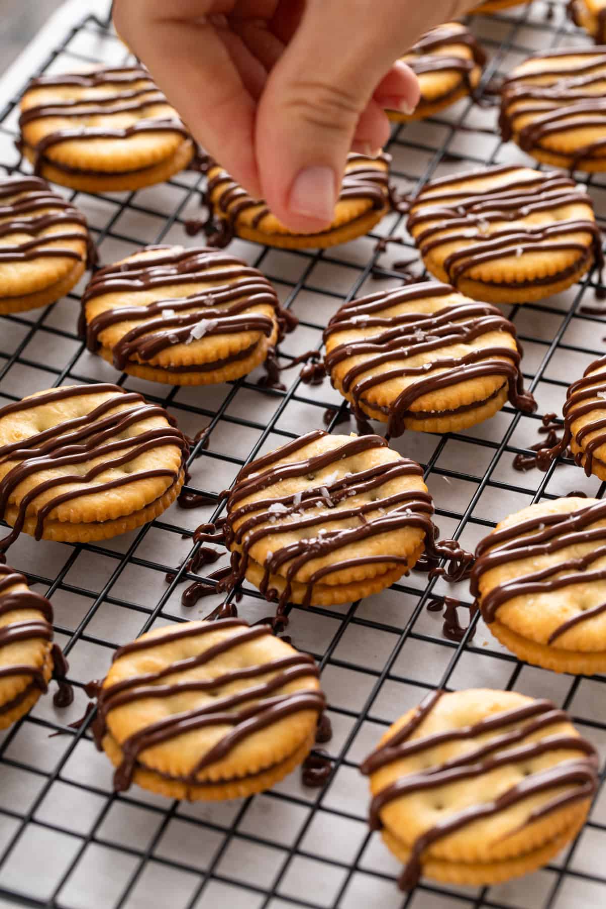Person sprinkling flaky salt over rolo ritz cracker cookies on a wire rack.
