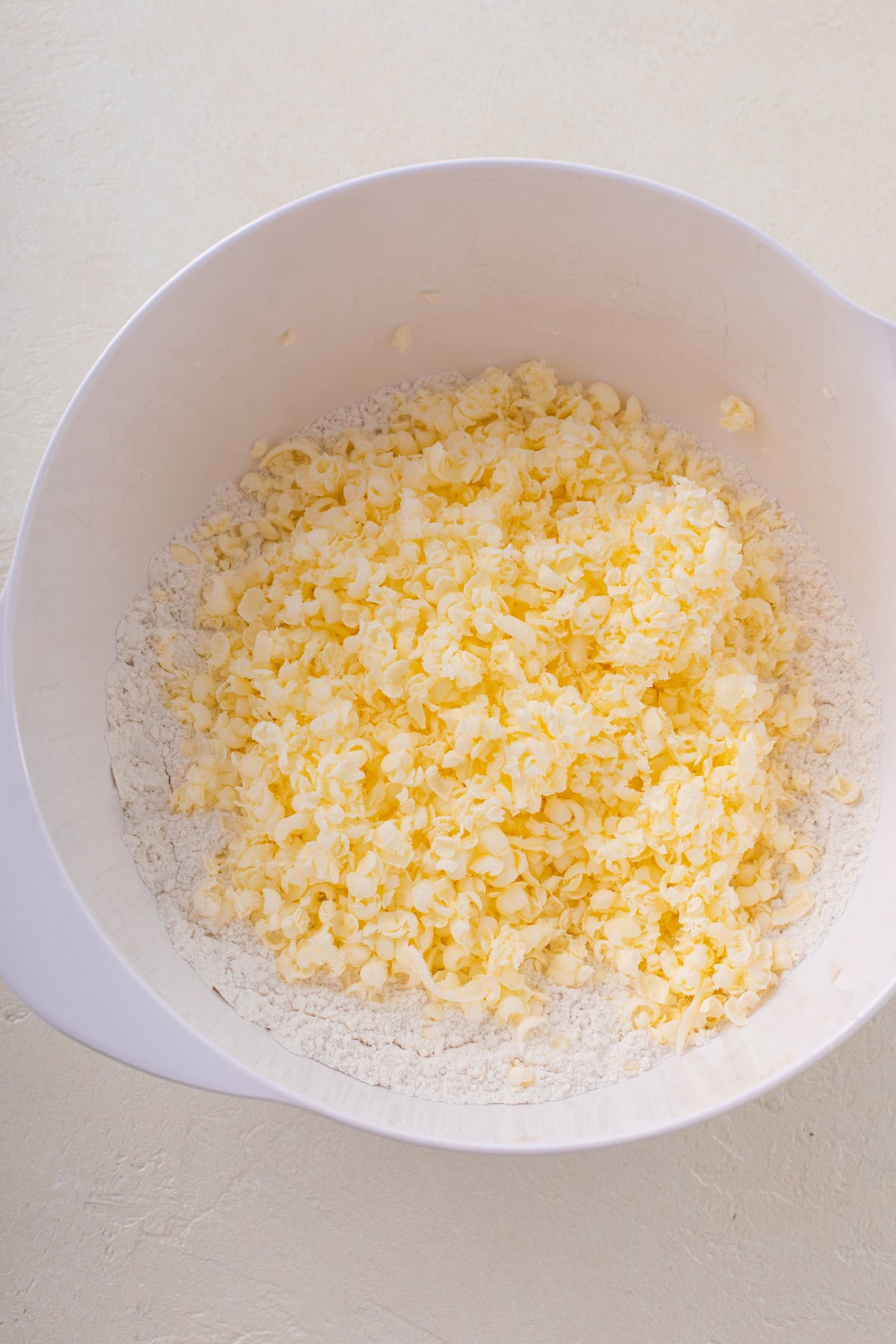 Grated butter added to dry ingredients for scones in a white bowl.