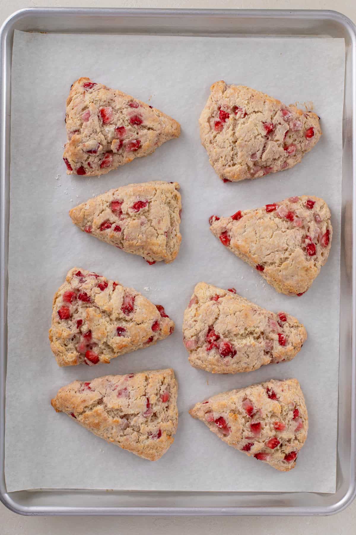 8 baked strawberry scones cooling on a parchment-lined baking sheet.