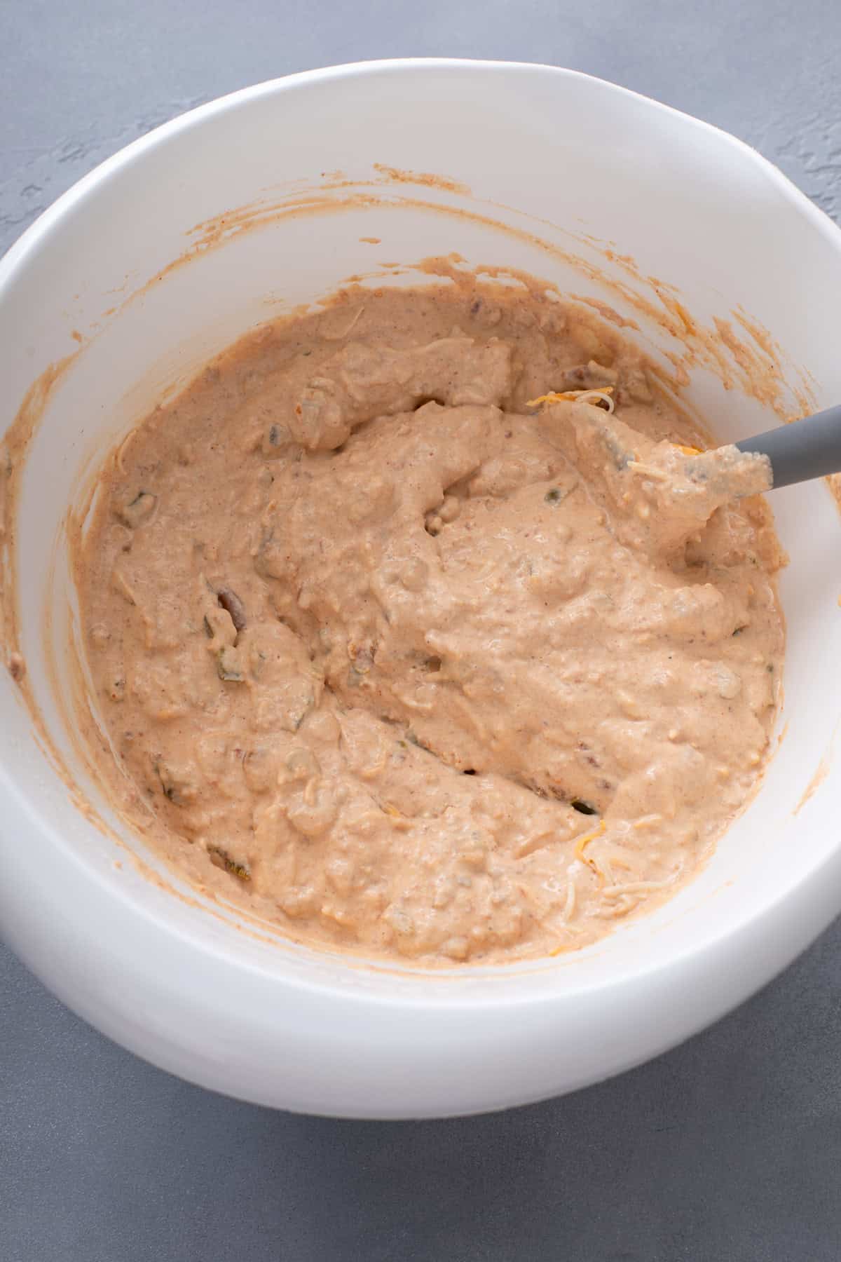 Bean mixture for texas trash dip mixed with a spatula in a white bowl.
