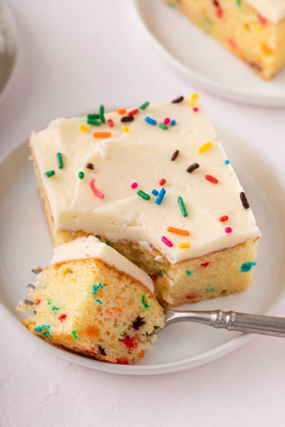 fork cutting a bite of cake from the corner of a slice of funfetti sheet cake.