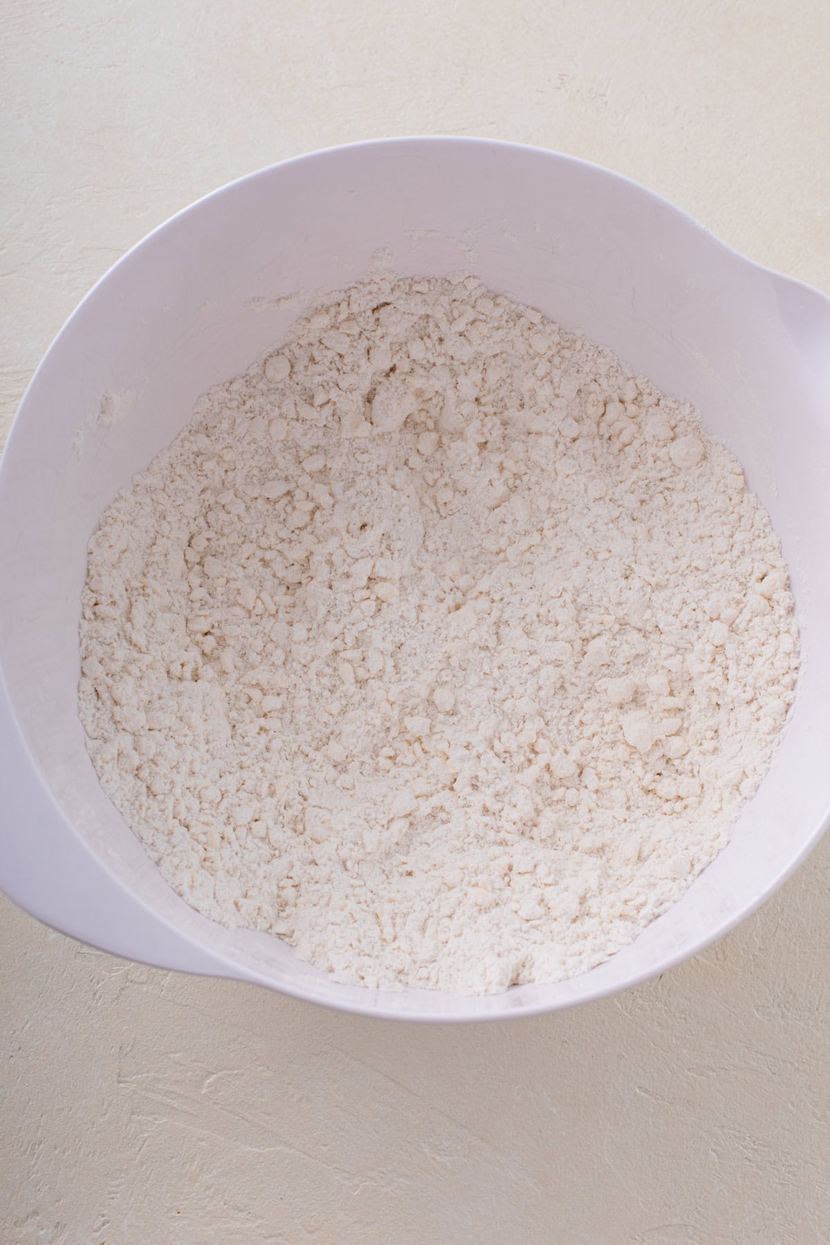 Butter worked into dry ingredients for scones in a bowl. The mixture resembles coarse meal.