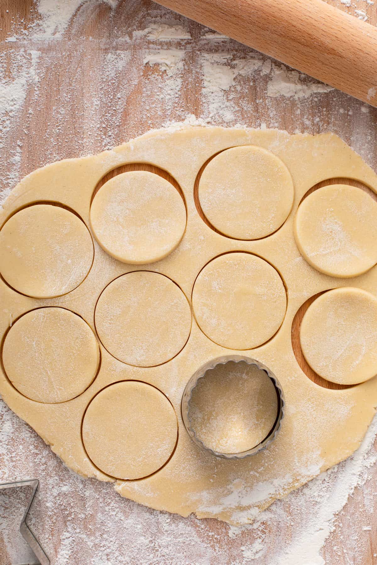 Circle cookie cutter cutting out rolled no-spread sugar cookie dough on a floured wooden board.