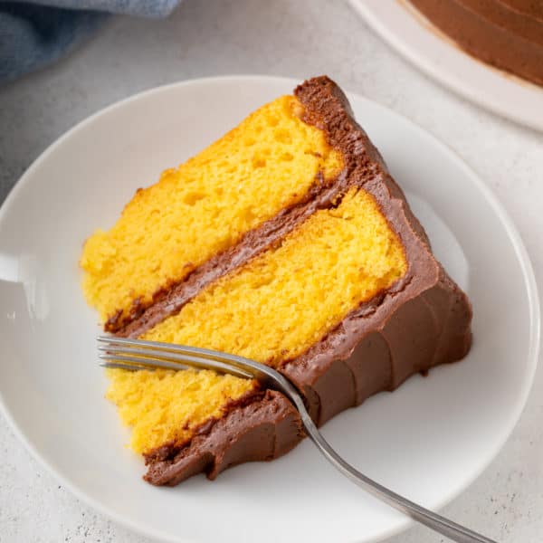Fork cutting a bite from a slice of yellow cake on a white plate.