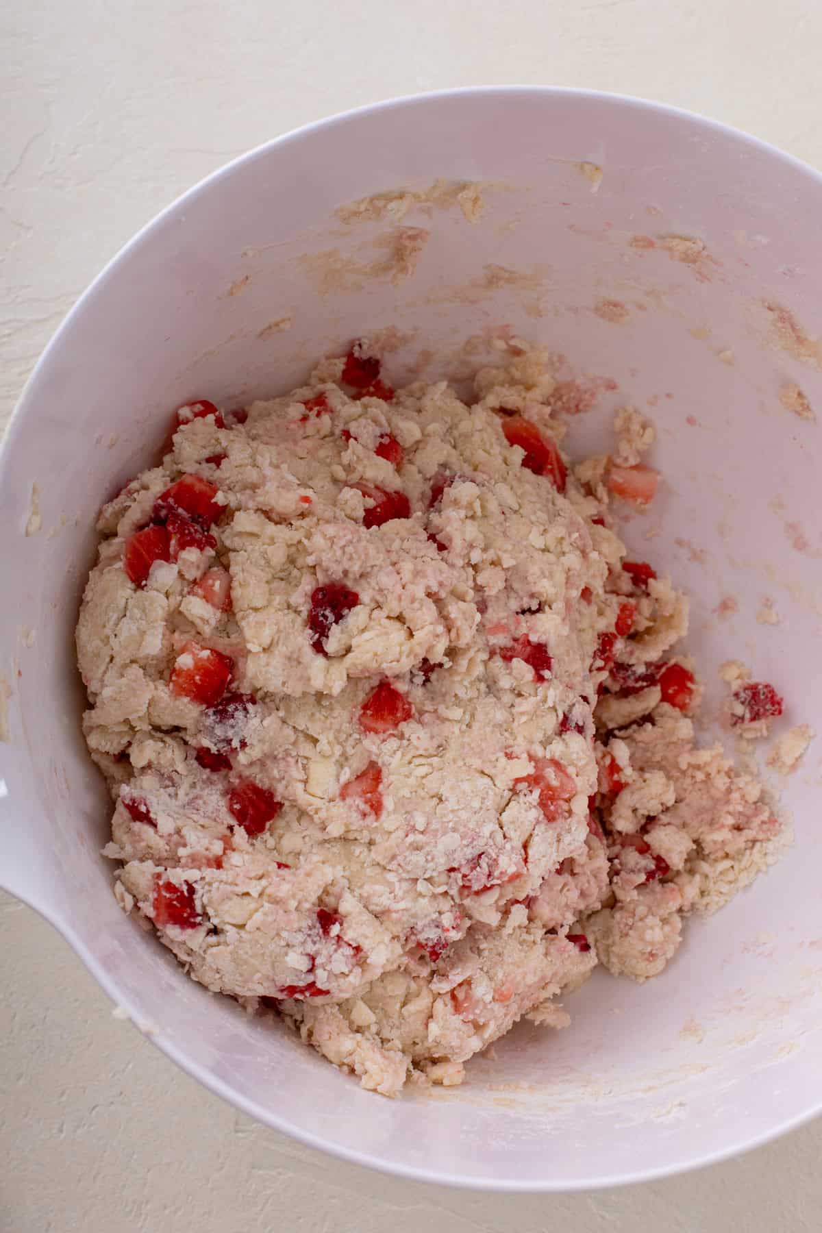 Mixed strawberry scone dough formed into a rough ball in a white bowl.