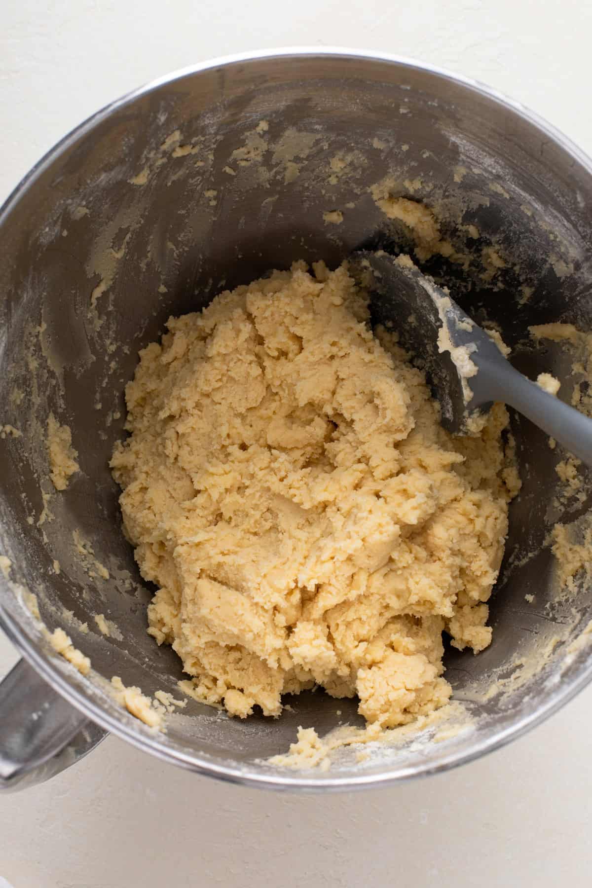 Spatula stirring no-spread sugar cookie dough in a metal mixing bowl.