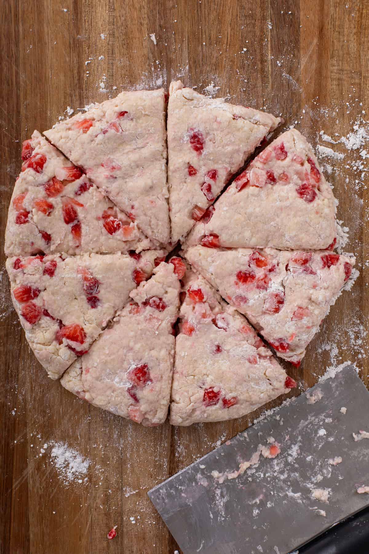Strawberry scone dough patted into a disk on a floured wooden board and cut into 8 wedges.
