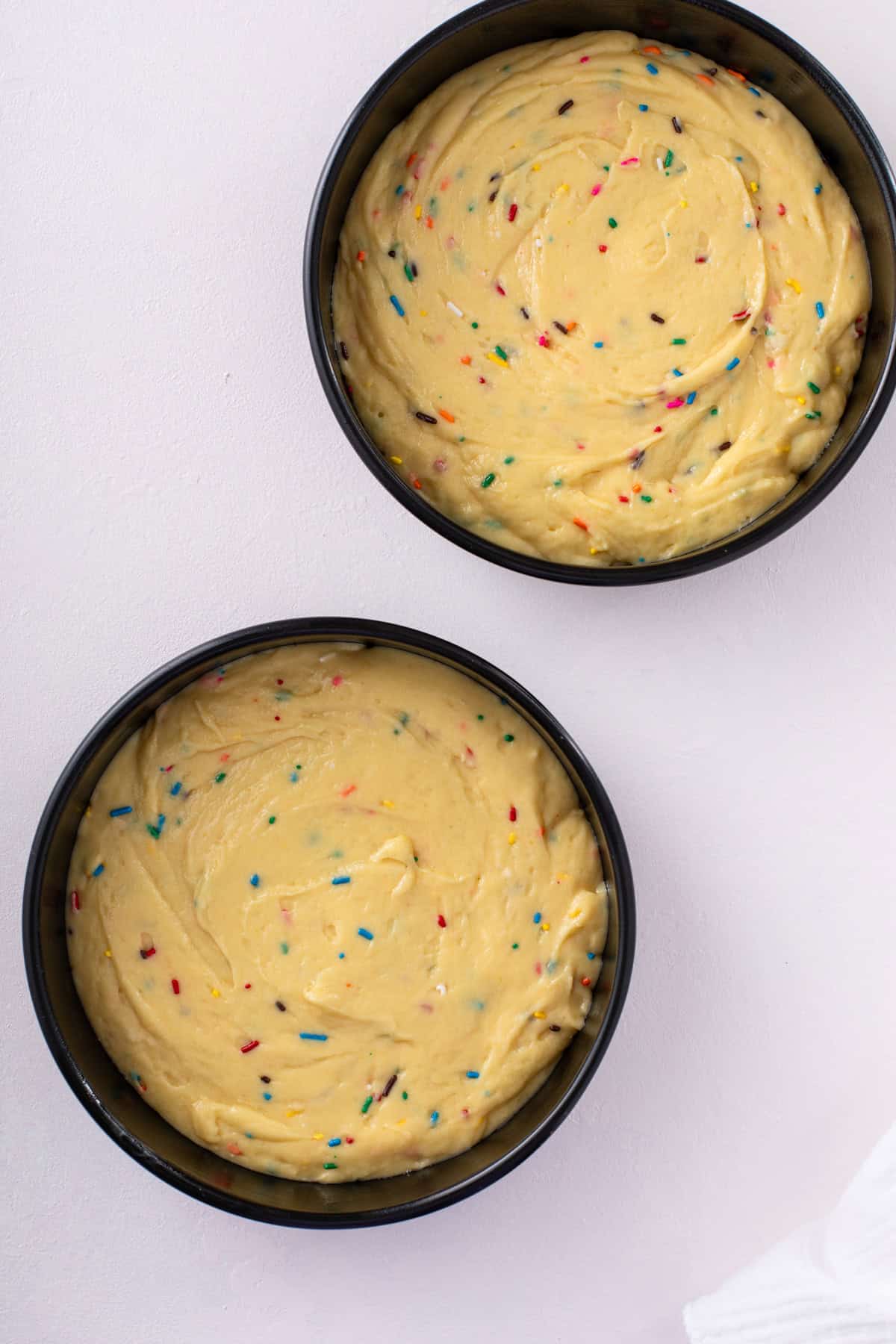 Easy funfetti cake batter divided between two round cake pans, ready to go in the oven.
