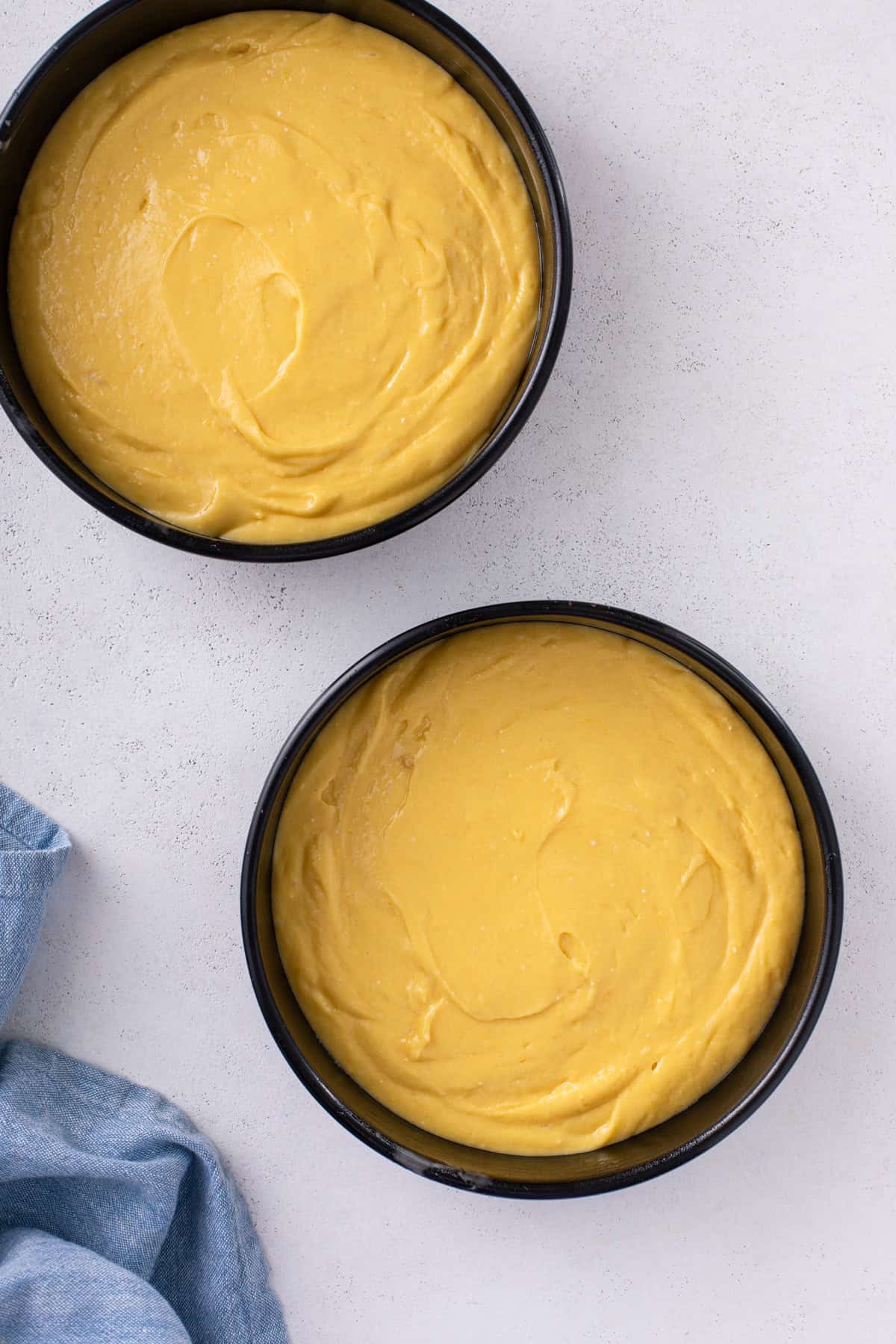 Two round cake pans each filled with easy yellow cake batter, ready to go in the oven.