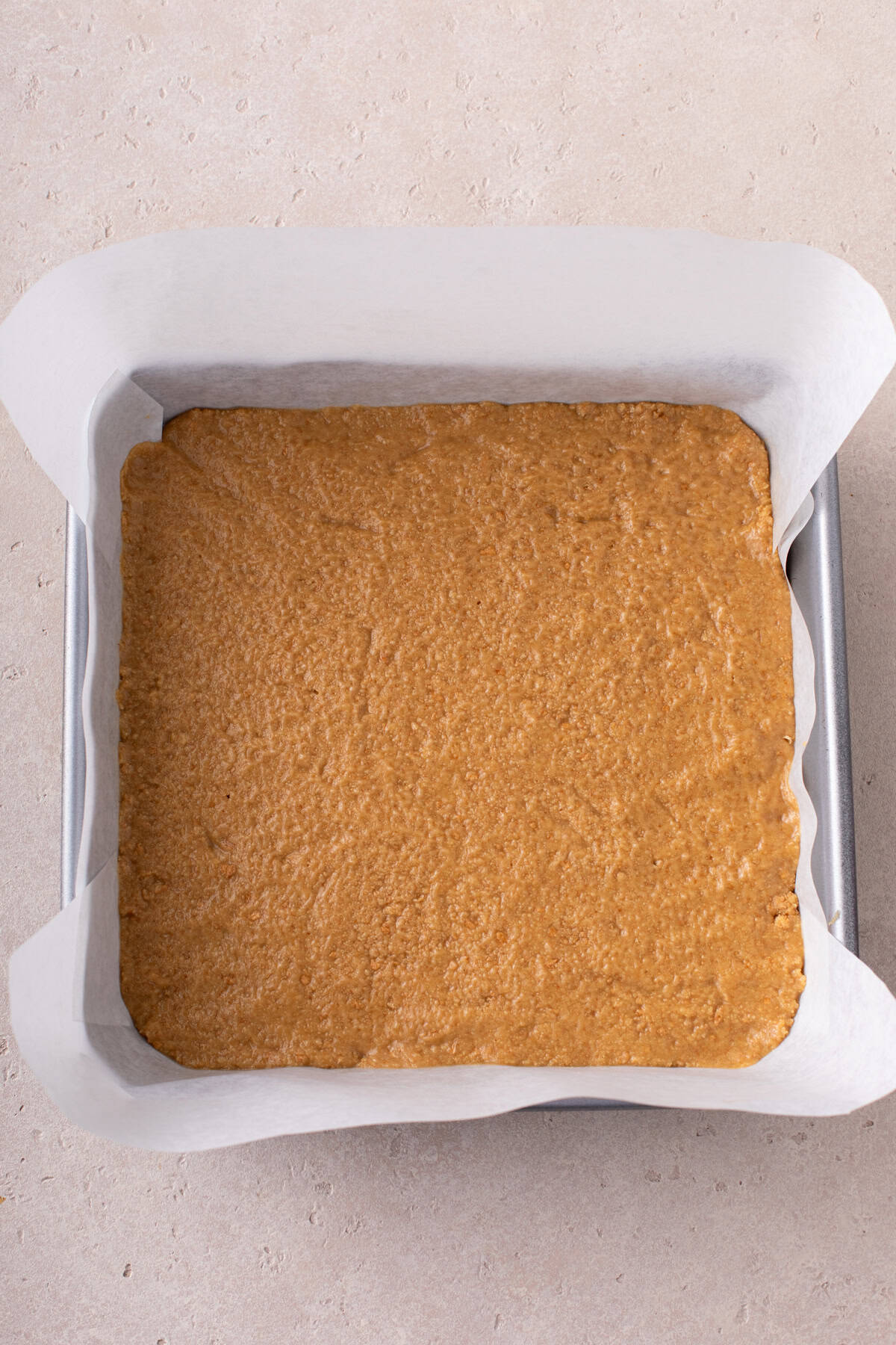 Peanut butter base for lunch lady bars pressed into a parchment-lined square pan.