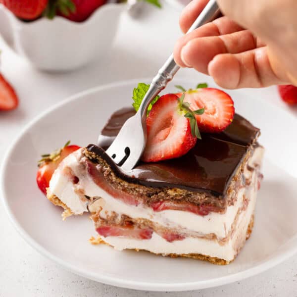 Person cutting in the corner of a slice of strawberry eclair cake with a fork.