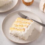 Slice of sour cream coconut cake next to a fork on a plate.