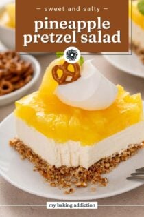 Close up of a plated slice of pineapple pretzel salad garnished with whipped cream, with a bite taken from the corner. Text overlay includes recipe name.
