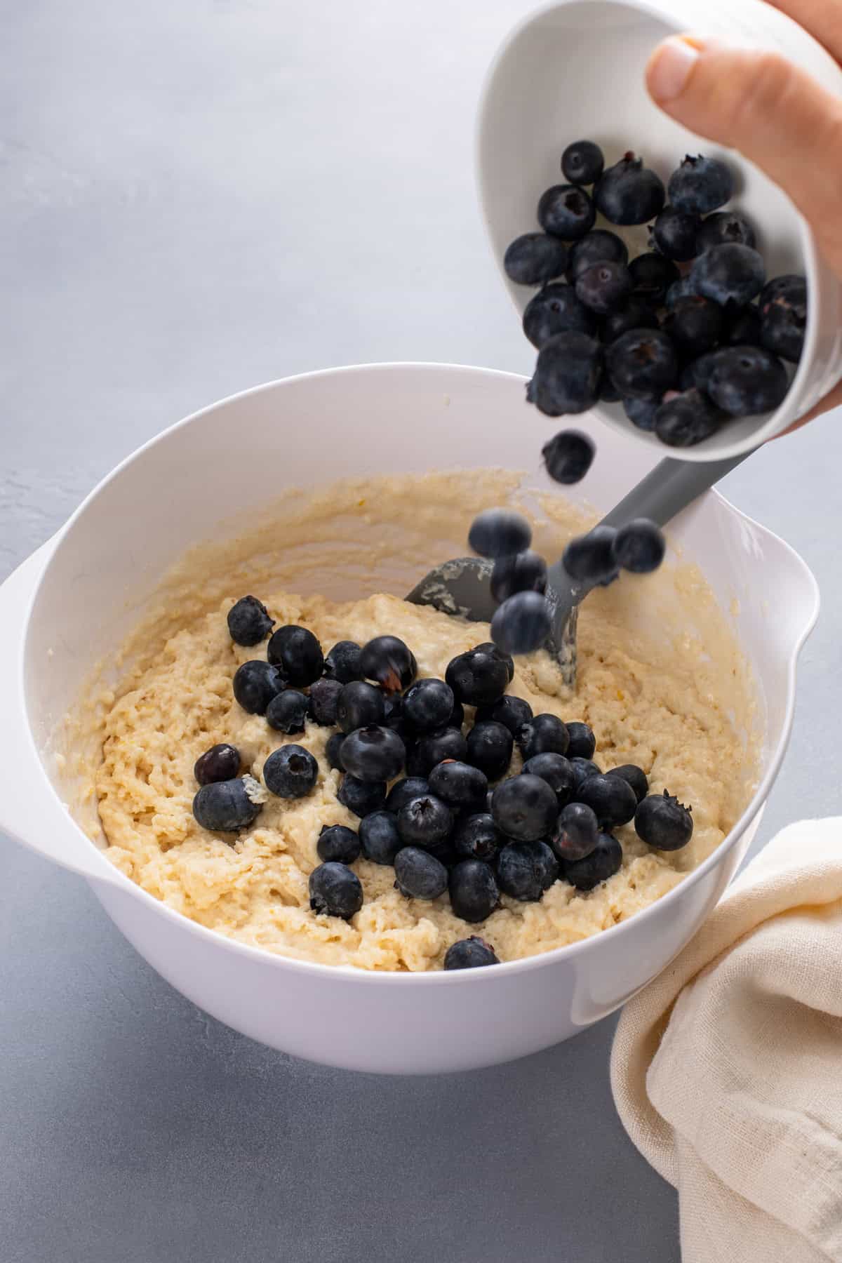 Fresh blueberries being added to muffin batter in a white bowl.